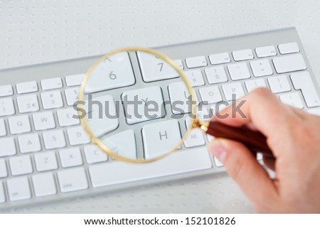 Close-up of hand looking at keyboard key through magnifying glass