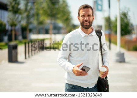 Businessman on street holding coffee and using phone