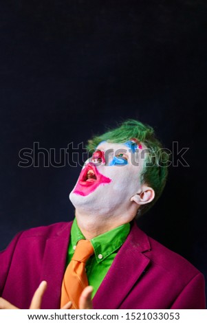 Man in mime makeup cosplay with green hair and a red suit an orange tie and a green shirt.