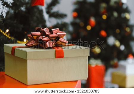 gift box with red ribbon on desk with christmas tree and bokeh light background, new year gift, holiday family celebration, happy new year and merry christmas festival concept, vintage tone effect
