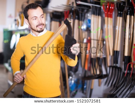 Young guy checks the quality of the hoe in the garden tools store