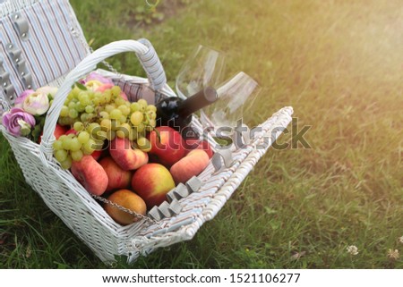 White wicker picnic basket with fruit and wine on the grass. Sunlight. Photo on the nature. Vacation concept. Top view.