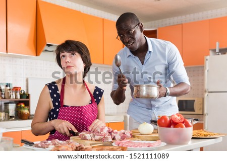 Portrait of bored woman cooking in home kitchen listening to reprimand from displeased husband