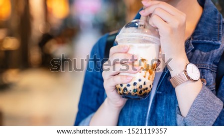 Young woman is holding, drinking brown sugar flavored tapioca pearl bubble milk tea with glass straw in night market of Taiwan, close up, bokeh Royalty-Free Stock Photo #1521119357