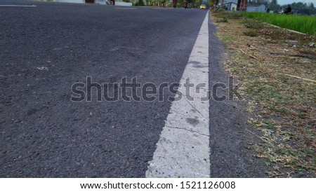 white curb line,
white line texture on asphalt road markers for road users.
soft and blur against the asphalt road and trees on the shoulder of the road