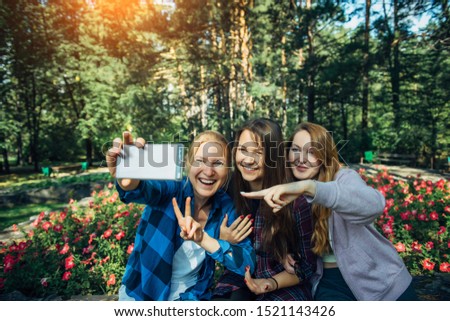 Portrait of cute girlfriends taking selfie with smartphone in summer park. Friendship, technology and people concept - happy young women having fun and taking photos for instagram.