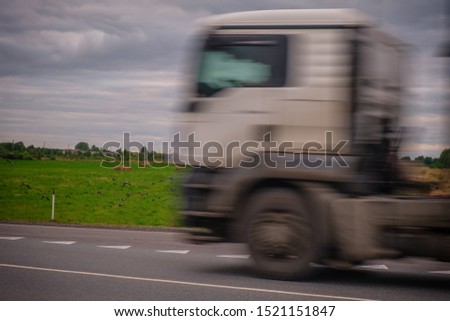 Silhouette of a blurred car at speed. A truck travels at high speed along a green field.