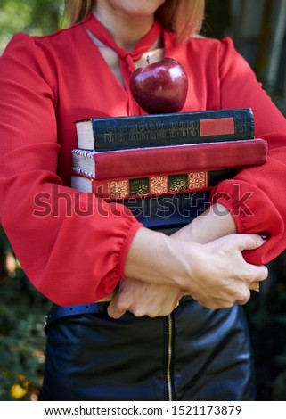 Close-up picture of hands, holding a bunch of books and red apple. Female student, wearing red shirt and black skirt, with many books in her hands. Study exams process. Education in college.