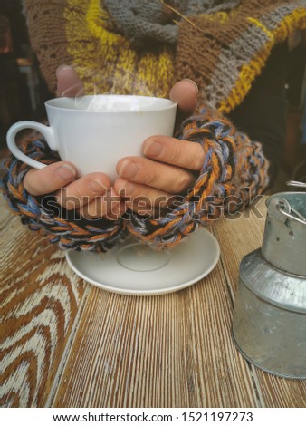 Lovely female hands holding a white Cup of hot coffee. Cozy photo of a Cup of coffee. A girl in a warm knitted sweater holding a Cup of hot coffee.
