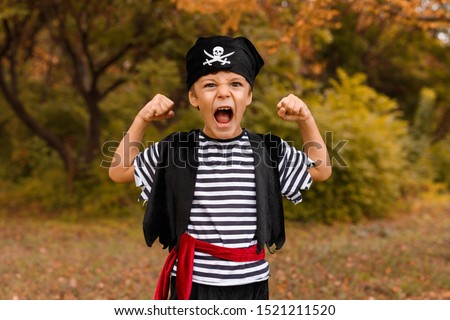 Funny little kid in carnival outfit standing in nature background with raised hands shouting and looking at camera on Halloween