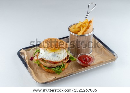 Juicy beef burger with fried egg and crispy french fries on a tray with craft paper isolated on white flat lay