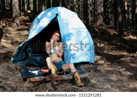 In the background young woman with red hair, camping with the tent in the woods