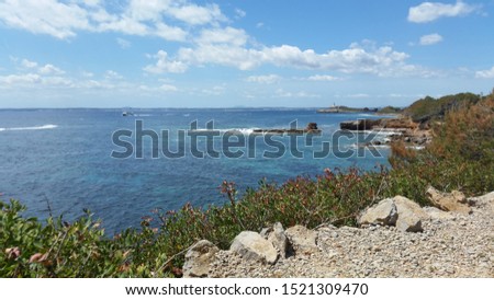 Picture of the coastline of Platja des Secs. Light blue water, a boat and a clear blue sky.
In the background you can see Platja d'Alcanada and the Lighthouse.

