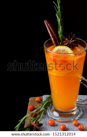 Fruit punch with sea buckthorn berries, citrus and spices in a tall glass on the edge of the table against black background