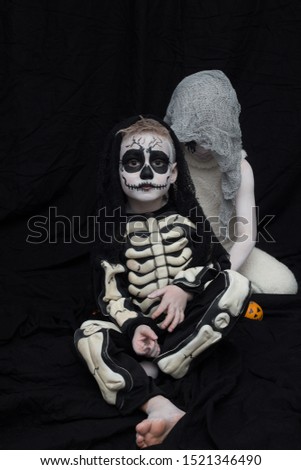 boys in halloween costumes. Clever, puzzled skeleton. A boy with an orange. Black studio background. ghost and skeleton friends.