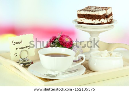Cup of tea with cakes on wooden tray on table in room 
