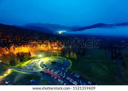 Aerial view from Unkai Terrace viewpoint in Hoshino Resort Tomamu at dusk, with cars in a parking lot and distant mountains veiled in the fog in blue twilight, in Shimukappu Village, Hokkaido, Japan