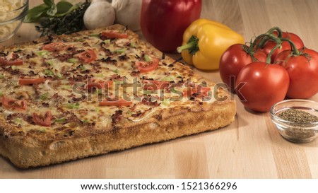 A closeup shot of a square-shaped pizza with fresh tomatoes, peppers, mushrooms and spices on a wooden surface