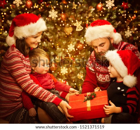 Christmas Family Open Present Gift Box in Home room, Parents with Children in Santa Hats front of Decorated Xmas Tree