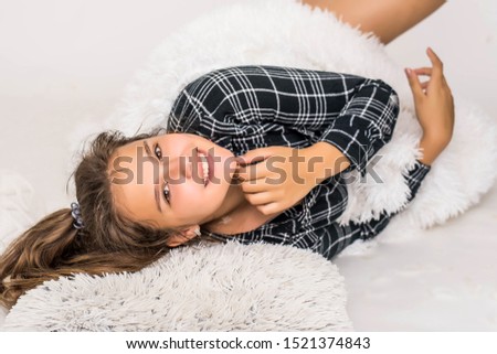 Cute teenage girl have fun on bed with feathers. Image of young smiling pretty lady lies in bed indoors.