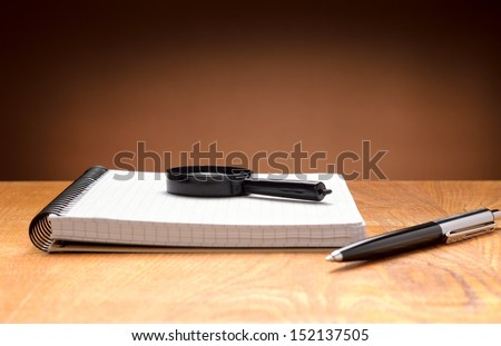 Notebook, pen and magnifier on a wooden background