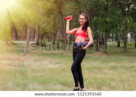 Young attractive smiling toned joyful brunette woman with dumbbells in a park. Healthy lifestyle concept