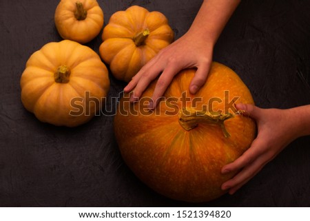 Pumpkins on black table. Halloween background with pumpkin. Human hands. Top view