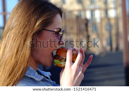 Beautiful girl in jeans clothes eating a Burger outside on a Sunny day