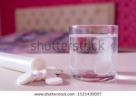 The effervescent tablet dissolves in a glass of water. A handful of pills on the table. Blurred background the bed in the bedroom. Treatment of viral diseases. Help with depression and insomnia