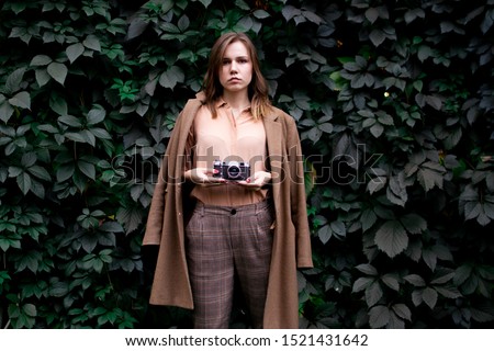 young beautiful girl photographer stands with a film camera near a wall of leaves in the forest, a woman photographs in nature