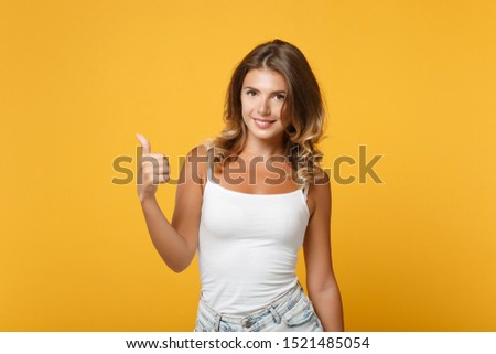 Beautiful young woman girl in light casual clothes posing isolated on yellow orange wall background, studio portrait. People sincere emotions lifestyle concept. Mock up copy space. Showing thumb up