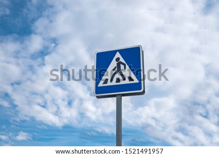 International traffic sign 'Pedestrian crossing'. Background contains cloudy blue sky