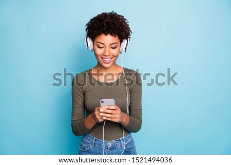 Photo of cheerful cute nice attractive trendy black girlfriend searching for new songs through her phone as answering people on social media isolated over blue vivid color background