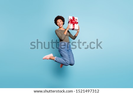 Full length body size photo of excited crazy cheerful nice positive ecstatic woman wearing jeans denim holding giftbox with hands jumping up isolated with vivid color blue background Royalty-Free Stock Photo #1521497312