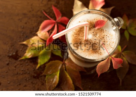 Autumn composition still life. Glass cup of coffee latte with cocktail straw and autumn colored leaves on wooden board with drops of water. View from above