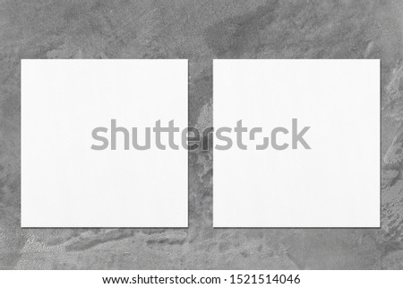 Two empty white square flyer or business card mockups with soft shadows on elegant dark grey concrete background. Flat lay, top view
