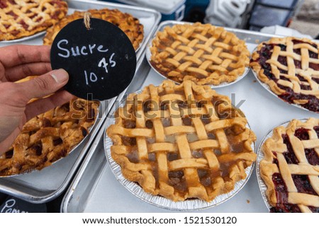 Baked goods at outdoor agriculture fair. A closeup view of a person holding a small French price sign, saying sugar, by a display of freshly baked sweet tartlets during a local farmer's fair.