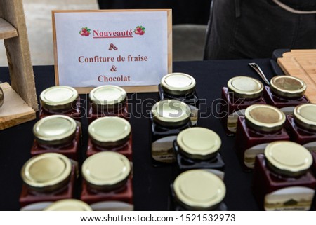 Fresh food at outdoor farmer's market. A closeup and high angled view on jars of strawberry jam and chocolate spread with a French sign, for sale during a fair for local food producers.