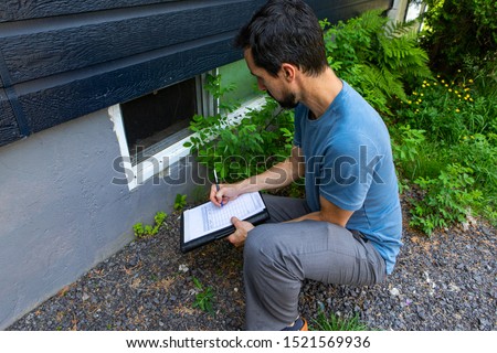 Indoor damp & air quality (IAQ) testing. A close up view on environmental home quality inspector at work, filling in a form as he inspects the exterior of a cellar window, with room for copy. Royalty-Free Stock Photo #1521569936