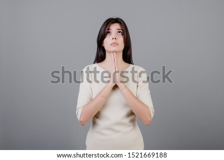 beautiful brunette woman praying and looking up isolated over grey