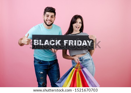 handsome young couple boyfriend and girlfriend with black friday sign and colorful shopping bags isolated over pink
