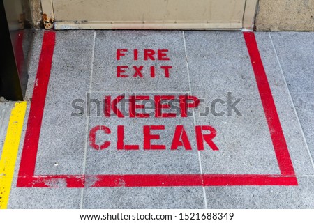 Fire Exit Keep Clear warning text and sign painted in red on concrete floor near the exit door from business office, residential building inform to keep the doorway accessible