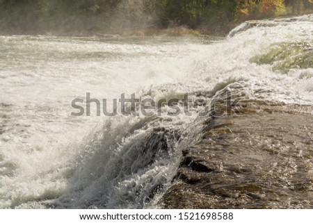 Early Fall Scenic picture of Healey Falls Peterborough Ontario Canada featuring gorgeous waterfalls with water streaming over rocks and water spray with a orange red vibrant leaves forest