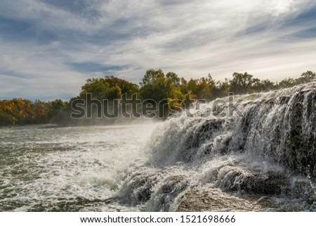 Early Fall Scenic picture of Healey Falls Peterborough Ontario Canada featuring gorgeous waterfalls with water streaming over rocks and water spray with a orange red vibrant leaves forest
