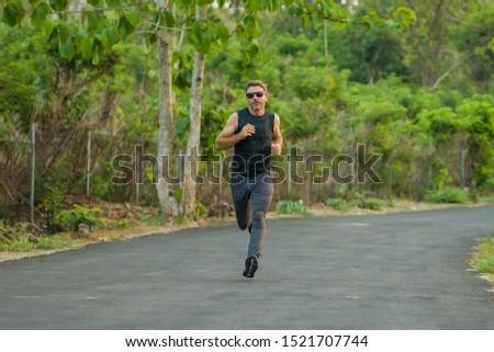 lifestyle portrait of young attractive and healthy man on his 30s or 40s running on country road doing jogging workout training happy on beautiful natural background in fitness and sport concept