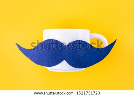 Blue paper mustache on a coffee mug on a bright yellow background. Contrasting colors, minimalism, flat lay, top view. 