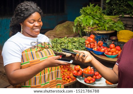 african woman in a market receiving payment via contactless transfer of funds from a customer using their mobile phones Royalty-Free Stock Photo #1521786788