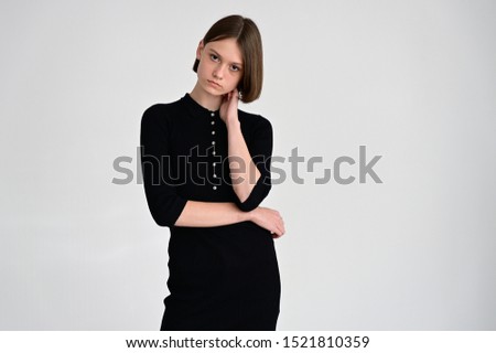 Portrait of a slim teenage girl on a white background in a black dress. Art, model posing.