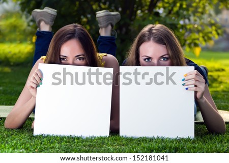 Happy young girls holding white blank papers against background of summer green park. Young girls showing blank boards. Female models portrait outside.