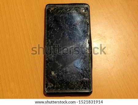 Smartphone with broken screen on the yellow wooden table